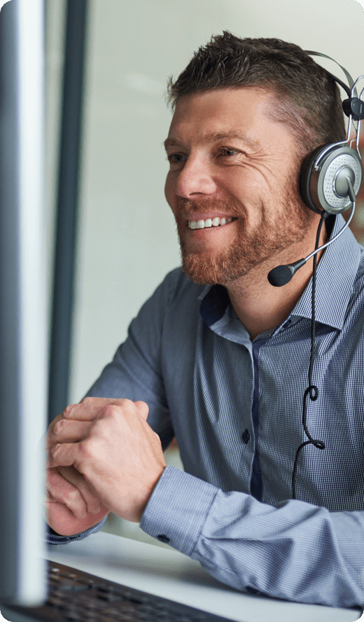 A smiling man in grey shirt looking at his desktop wearing headphones