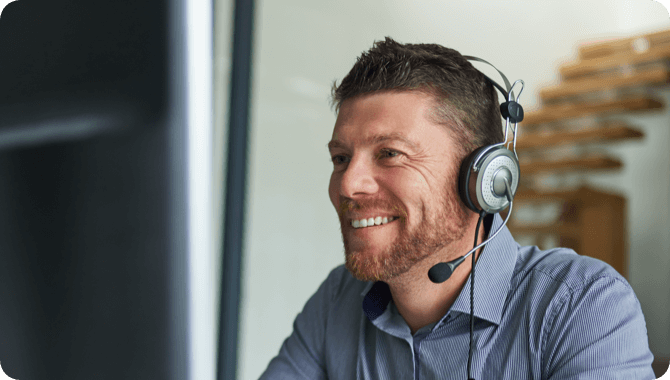 A smiling man in grey shirt looking at his desktop wearing headphones