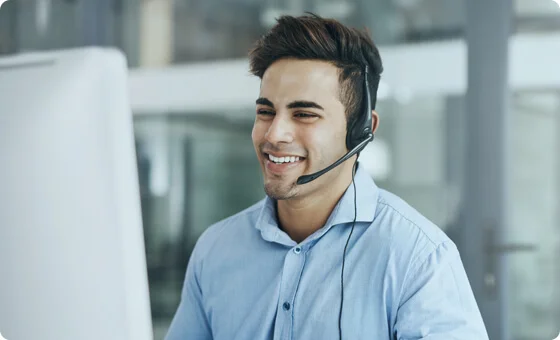 A young man wearing headphones and smiling at the desktop.